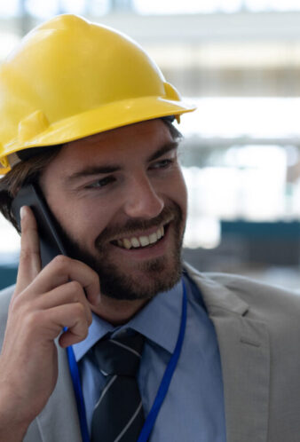 Front view of happy handsome male architect talking on mobile phone in modern office